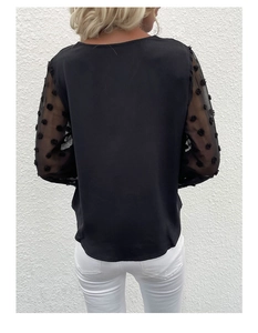 Detail view of women black top featuring sheer mesh sleeves with textured polka dots
