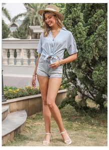 Scatto all'aperto di una donna con camicia annodata blu chiaro e pantaloncini di jeans