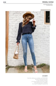 Outdoor street view of a woman wearing a navy polka dot long sleeve top and blue jeans