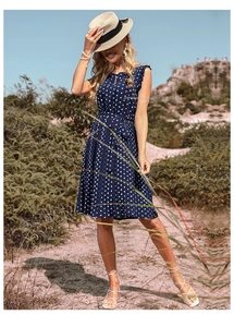 Detailed view of navy polka dot pleated dress featuring a tie waist and ruffle sleeves