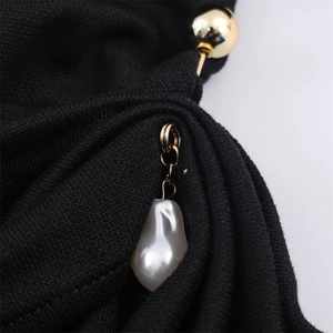 Detalle de vestido de punto negro con pasador dorado y colgante de perla barroca