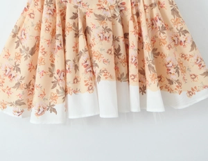 Dettaglio di abito floreale in chiffon con pieghe color pesca e bordo bianco