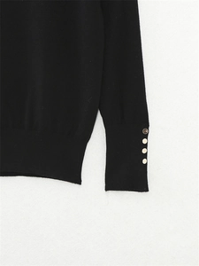 Detail of a black knit sweater cuff with decorative gold buttons on a white background