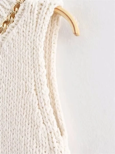 Close-up of white chunky knit top featuring a bold gold chain detail on the neckline