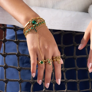 Close-up detail of luxury gold-plated hand chain set with emerald green zircon crystals