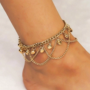 Macro view of a stylish gold-colored multi-layer anklet featuring bells and hearts