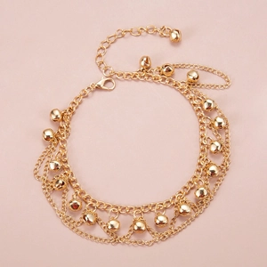 Detailed macro view of a layered gold anklet with bell charms on a pink background