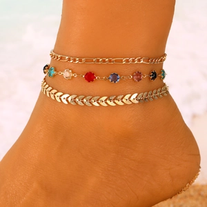 Dreiteiliges goldenes Fußkettchen-Set mit Evil Eye Anhängern am Strandhintergrund