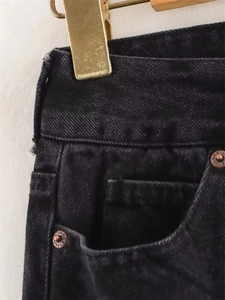 Macro detail of black denim jeans showing waistband stitching and bronze rivets with engraving