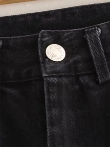 Close-up of metal button with embossed text on washed black denim jeans waist detail