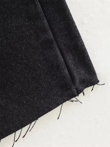 Detailed close-up of dark grey denim fabric showing raw hem and twill texture