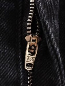 Detailed macro view of retro metal zipper with A+K engraving on black denim jeans