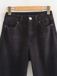Close-up detail of high-waist black washed denim jeans with silver button and rivets