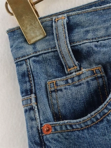 Détail de la taille en jean bleu avec rivets en cuivre et doubles coutures orange