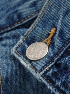 Gros plan d'un bouton métallique sur un jean denim bleu foncé délavé avec logo GEE JAY