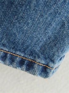Vue détaillée du tissu denim délavé bleu avec coutures jaunes et bords effilochés