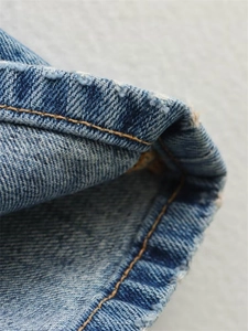 Détail macro de l'ourlet en denim montrant des coutures orange et une texture délavée