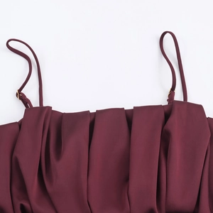 Détail macro du décolleté plissé bordeaux avec fines bretelles et boucles dorées