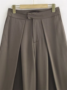 Détail montrant les plis profonds et la texture lisse du pantalon large marron foncé