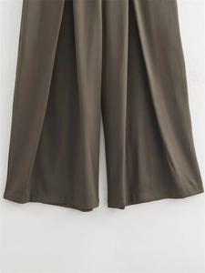 Détail d'un pantalon large olive foncé avec plis élégants et tissu au drapé soyeux
