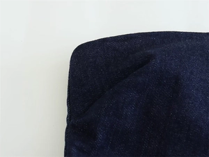 Close-up of dark blue denim fabric texture showing detailed twill weave and neat stitching