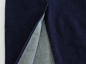Detail view of denim dress slit design with precise stitching and twill texture