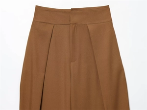 Detail view of double pleated waistband and fine stitching on brown high-waist trousers
