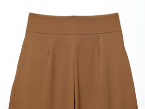 Detail of high-waist pleated design on brown trousers with precise darts and smooth texture