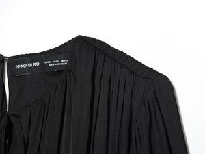 Détail macro du décolleté plissé noir avec étiquette de marque et informations de taille