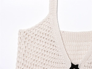 Detailansicht des cremefarbenen Stricktops mit Netzstruktur und schwarzer Schleifenverzierung