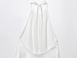 Detalle de top de satén blanco con cuello halter, pliegues finos y lazo al cuello