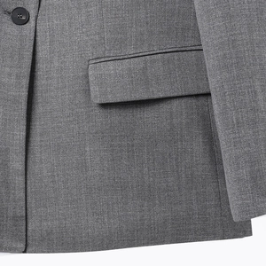 Detalle de blazer gris de espiga que muestra el botón de resina negra y el bolsillo de solapa