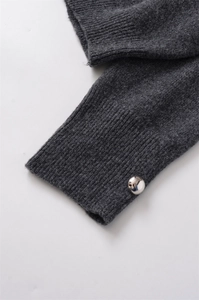 Détail du poignet en maille gris foncé avec texture côtelée et bouton argenté brillant