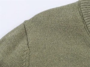 Close-up detail of the olive green knit sweater showing ribbed crew neck and shoulder seams