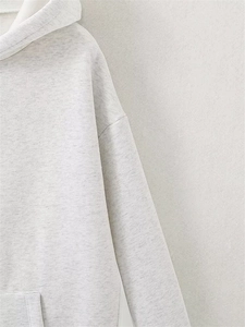 Detailed close-up of light grey heather fabric texture on a loose hooded sweatshirt