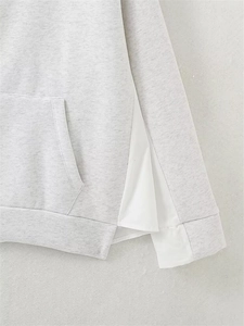 Detail of light gray knitted hoodie showing side white fabric patchwork and kangaroo pocket