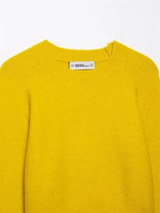 Close-up of vibrant yellow knit sweater featuring a soft wool-like texture and brand neck label