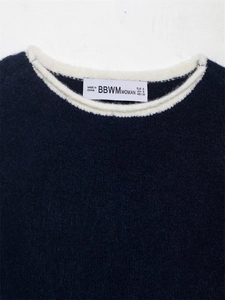Détail du col rond contrasté blanc sur le pull en maille bleu foncé avec étiquette