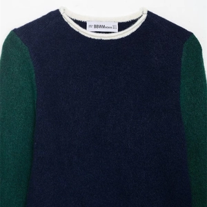 Pull en maille contrastée avec col rond, corps bleu marine et manches vertes sur fond blanc