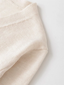Detailaufnahme der feinen Strickstruktur und Nähte eines cremefarbenen V-Pullovers