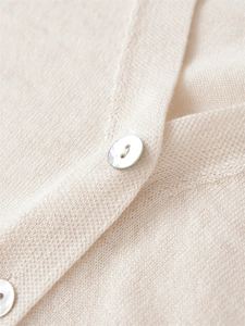 Makro-Detail von feiner Stricktextur und Perlmuttknöpfen an einer beigen V-Strickjacke