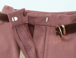 Dettaglio vita con bottone in resina e cintura in pelle di coccodrillo su pantaloni rosa