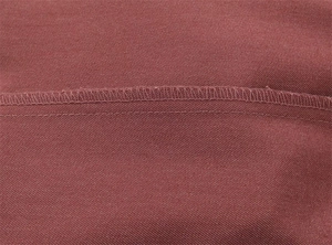 Macro dettagliata di cuciture rinforzate e punti overlock su tessuto rosso-marrone