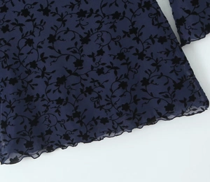 Detail of blue sheer mesh fabric with black flocked floral pattern and lettuce hem