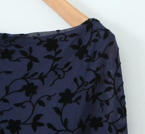 Detail of dark blue mesh dress with black flocked floral patterns on a wooden hanger
