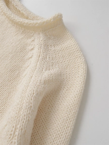 Détail d'un pull en maille crème montrant le mélange de laine et le col rond roulé