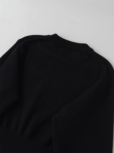 Detail view of the crew neck and fine knit texture of a black long-sleeved sweater
