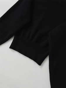 Detail view of the fine knit texture and ribbed hem on a classic black sweater