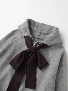 Detail view of a grey knit hoodie featuring a large brown bow tie and silver zipper hardware
