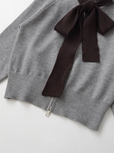 Detail of grey knit hoodie with a contrasting dark brown bow and silver zipper puller